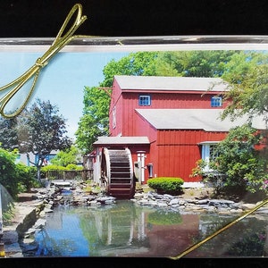 May include: A red wooden building with a water wheel in front of it. The building is surrounded by green trees and a small pond with blue water.