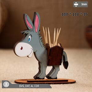 Puede incluir: Un palillero de madera con forma de burro. El burro es gris con orejas forradas de rosa, un hocico blanco y un recipiente de madera marrón en la espalda. Mide 100 x 118 x 35 mm. La base tiene el texto "SVG, DXF, AI, CDR".