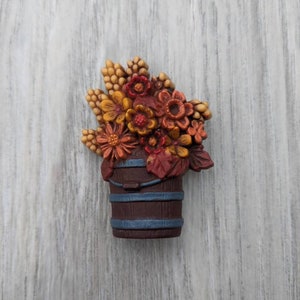 Puede incluir: Un arreglo floral de cerámica de estilo vintage en un cubo marrón y azul. Las flores son una mezcla de rojo, naranja y amarillo.