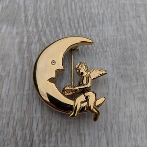 Gold Tone and Rhinestone Cherub Sitting on a Crescent Moon Trembler Brooch