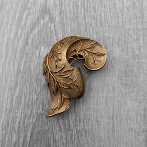 May include: A gold-toned brooch in the shape of a stylized leaf with intricate details.