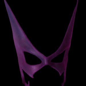 May include: A purple masquerade mask with a pointed, triangular shape and eye holes. The mask is made of a translucent material.