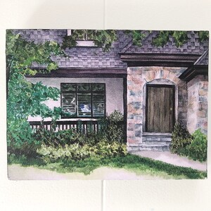 May include: A watercolour painting of a house with a stone facade and a wooden door. The house has white trim and a green roof. There are bushes and trees in front of the house.