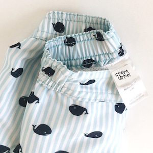May include: Blue and white striped swim trunks with a whale pattern. The trunks have an elastic waistband and a label that reads "Steve Urkel" with the text "Medium/Medium" and "4-5 yrs" underneath.