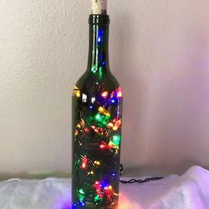 May include: A green glass wine bottle with a cork top filled with colorful string lights. The lights are red, green, blue, and yellow.