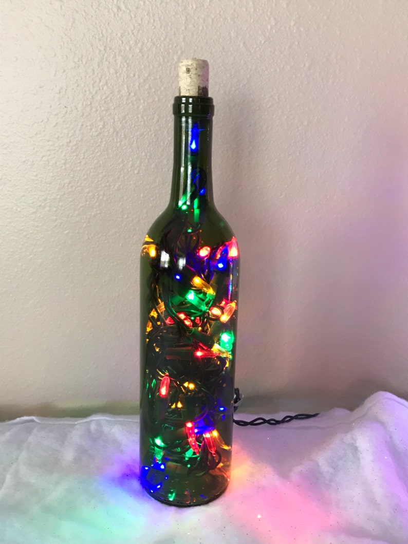 May include: A green glass wine bottle with a cork top filled with colorful string lights. The lights are red, green, blue, and yellow.