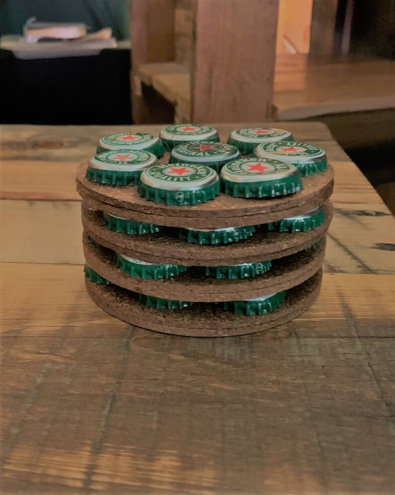 May include: A stack of brown cork coasters with green bottle caps on top. The bottle caps have a red star and the words "Original Quality" printed on them.