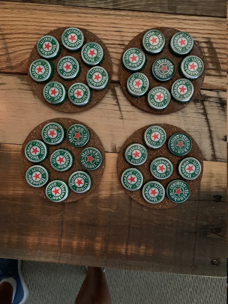 May include: Four cork coasters with a circular design featuring Heineken bottle caps. Each coaster has 10 bottle caps arranged in a circular pattern.
