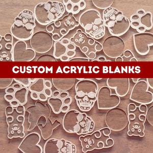 May include: A collection of clear acrylic blanks in various shapes, including skulls, teddy bears, hearts, paw prints, and circles. The text "CUSTOM ACRYLIC BLANKS" is displayed on a red banner across the image. These blanks are ideal for crafting.