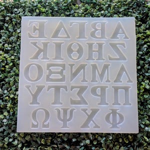 May include: White silicone mold with raised letters of the Greek alphabet. The letters are arranged in four rows of six letters each. The letters are uppercase and in a traditional font.