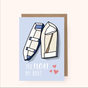 May include: An illustrated card featuring two boats in blue and white with the text "You float my boat" and three pink hearts.