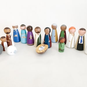 Könnte beinhalten: Ein Set aus Holz-Steckpuppen, die die Weihnachtsgeschichte darstellen. Die Puppen sind in verschiedenen Farben bemalt, darunter Braun, Blau, Grün, Rot und Weiß. Das Set enthält Maria, Josef, das Jesuskind, einen Esel, ein Schaf und mehrere andere Figuren.