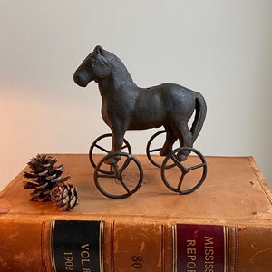 May include: A vintage cast iron toy horse with wheels sits on top of two leather-bound books. The books are titled "Mississippi Reports" and "Missouri Appeal Reports".