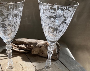 May include: Two clear glass wine glasses with etched floral designs on a wooden surface.