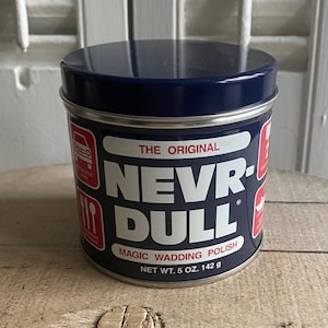 Op de afbeelding: Een marineblauwe metalen blik van "NEVR-DULL" magic wadding polish. De blik heeft een zilveren rand en een marineblauwe deksel. Het etiket is wit en rood, met de tekst "NEVR-DULL". Netto gewicht: 142 g.