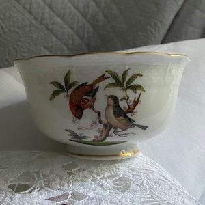 May include: A white porcelain bowl with a gold rim and a hand-painted design of two birds on a branch. The birds are a red and brown bird and a blue and white bird.