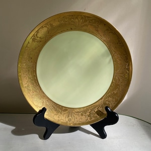 May include: A vintage porcelain plate with a pale green center and a gold rim with a floral design.