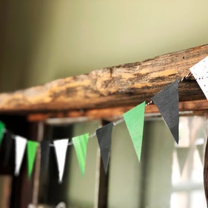 Puede incluir: Una cadena de banderas triangulares de papel en negro, blanco y verde cuelga de una viga de madera r&uacute;stica. Las banderas est&aacute;n decoradas con lunares blancos.
