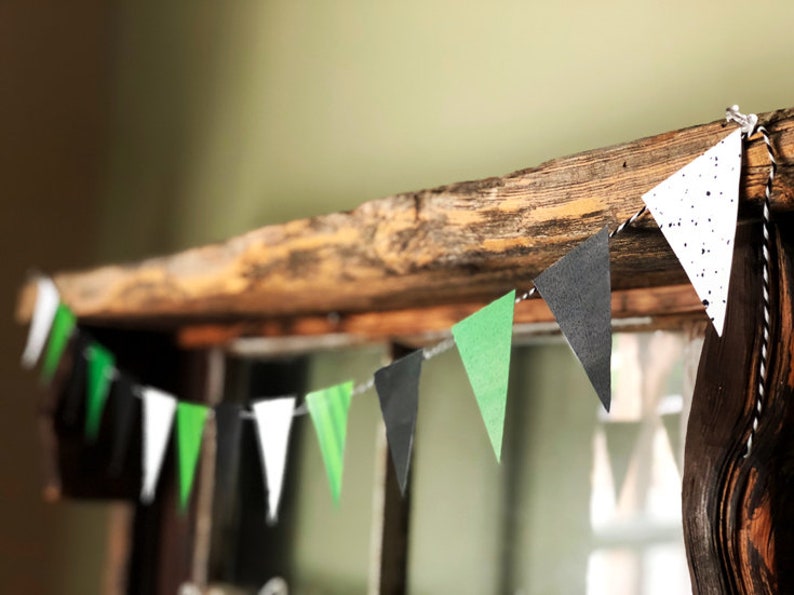 Puede incluir: Una cadena de banderas triangulares de papel en negro, blanco y verde cuelga de una viga de madera r&uacute;stica. Las banderas est&aacute;n decoradas con lunares blancos.