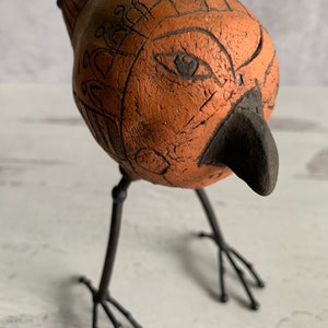 May include: A ceramic bird sculpture with a brown body and black legs. The bird has a detailed face with a black eye and beak.