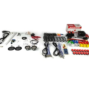 Può includere: Un set di componenti per giochi arcade che include un joystick, pulsanti, altoparlanti, LED e cablaggio. I componenti sono disposti su una superficie bianca. La scatola del joystick è etichettata "JOYSTICK".