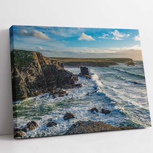 May include: A panoramic view of a rocky coastline with crashing waves. The sky is a bright blue with white clouds. The water is a deep blue with whitecaps. The rocks are a dark grey and brown.