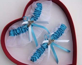 May include: Two blue and white garters with silver charms in a red heart-shaped box. The garters are made of white lace and blue satin ribbon.