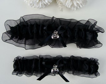 May include: Two black garters with a silver pumpkin charm. The garters are made of black satin and tulle.