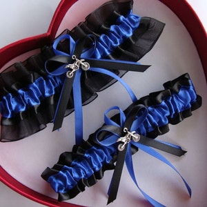May include: Two blue and black garters with silver motorcycle charms. The garters are displayed in a red heart-shaped box.