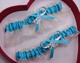 May include: Two white and turquoise garters with silver double heart charms. The garters are in a red heart-shaped box.