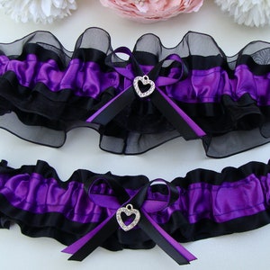 May include: Two purple and black garters with a rhinestone heart charm. The garters are made of satin and lace.