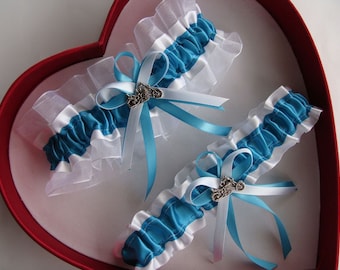 May include: Two white and teal blue garters with silver charms. The garters are made of satin and lace.