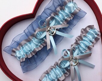 May include: Two blue and gray bridal garters with silver anchor charms. The garters are made with satin ribbon and tulle.