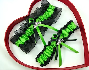 May include: Two black and green garters with a silver motorcycle charm. The garters are displayed in a red heart-shaped box.