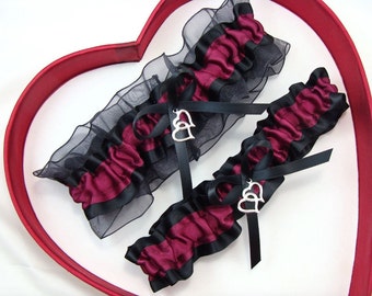May include: Two black and burgundy garters with silver double heart charms. The garters are made of satin and lace.