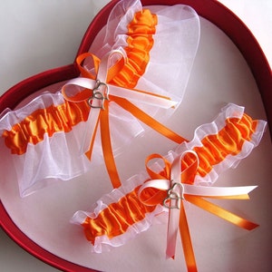 May include: Two white and orange bridal garters with silver heart charms in a red heart-shaped box.