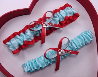May include: Two blue and red garters with a silver heart and key charm. The garters are on a red heart-shaped box.