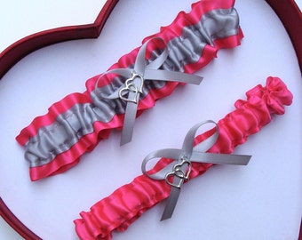 May include: Two bridal garters with a silver double heart charm. One garter is pink satin with a silver trim. The other garter is silver satin with a pink trim.