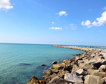 May include: A rocky shoreline extends into a turquoise ocean under a bright blue sky with white clouds.