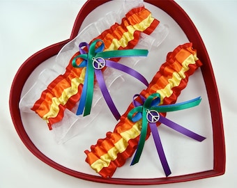 May include: Two rainbow-colored garters with ruffled edges, accented with green, blue, and purple ribbons, and a silver peace symbol charm. The garters are presented in a red heart-shaped box with a white interior.