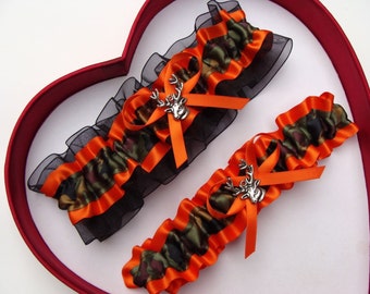May include: Two bridal garters with a camouflage and orange satin ribbon design. Each garter features a silver deer charm.