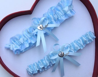 May include: Two light blue satin garters with silver key and heart charms. The garters are displayed in a red heart-shaped box.