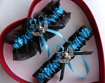 May include: Two blue and black garters with a silver skull charm and wings. The garters are displayed in a red heart-shaped box.