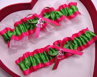 May include: Two white and pink garters with green satin ribbon and silver double heart charms. The garters are displayed in a red heart-shaped box.
