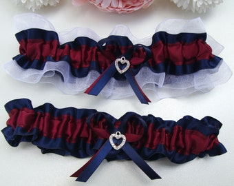 May include: Two bridal garters with a navy blue and burgundy satin ribbon design. Each garter features a silver heart charm with rhinestones.