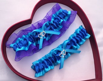 May include: Two blue and purple bridal garters with silver double heart charms. The garters are made with satin ribbon and lace.