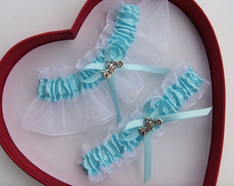 May include: Two blue and white garters with silver motorcycle charms. The garters are displayed in a red heart-shaped box.