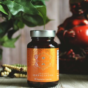 K&ouml;nnte beinhalten: Eine braune Glasflasche mit einem silbernen Deckel, die 60 vegetarische Kapseln mit Bio-Ashwagandha enth&auml;lt. Die Flasche hat ein goldenes Etikett mit den Worten "True Veda" und "Organic Ashwagandha" darauf.