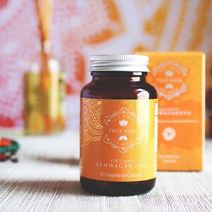 May include: A brown glass bottle with a silver lid containing 60 vegetarian capsules of organic Ashwagandha. The bottle has a gold label with the text "True Veda" and "Your Health Our World".