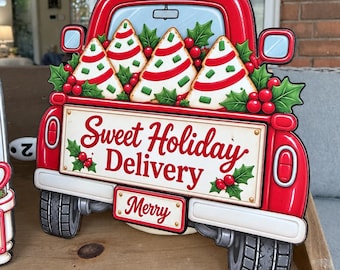 May include: A red metal truck sign featuring a bed filled with decorated triangular cookies, green holly leaves, and red berries. The tailgate displays the text Sweet Holiday Delivery in red script, and the license plate reads Merry in red.